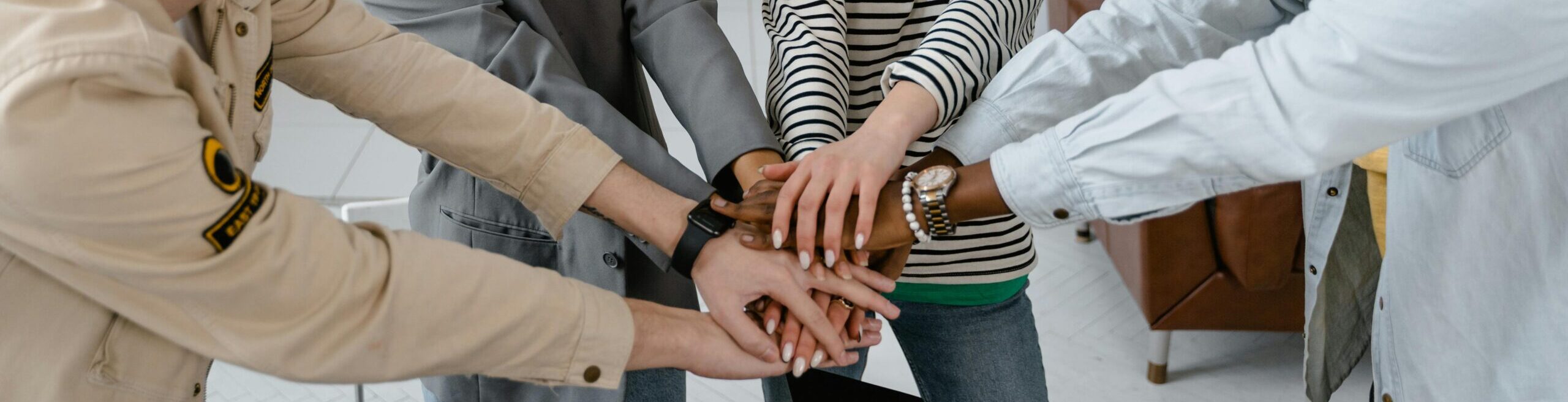 A group of diverse coworkers uniting hands to symbolize teamwork in a modern office.